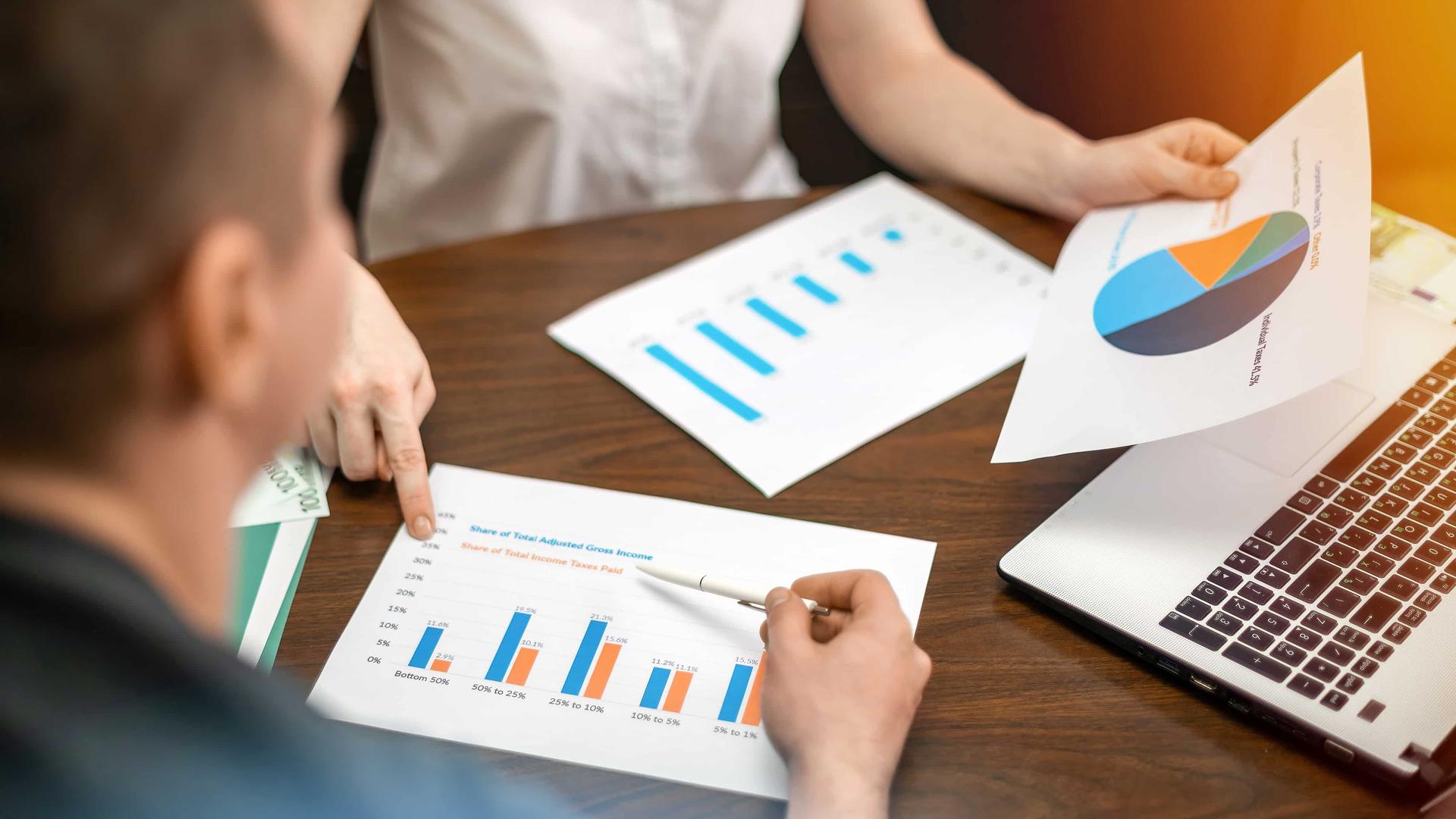 woman-showing-man-finance-diagrams-table-laptop-papers-min