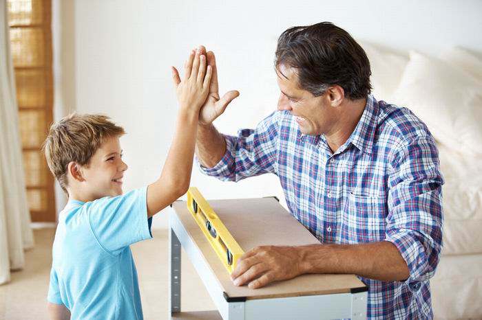 Excited man giving high five to a little boy after completing the work in workshop